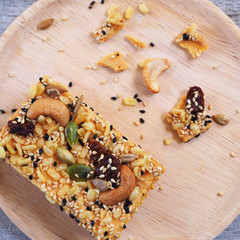 Top view of healthy crispy cereal bar or muesli bar with pumpkin seeds, sunflower seed, sesame, nuts and dried fruits with honey in a wooden plate.