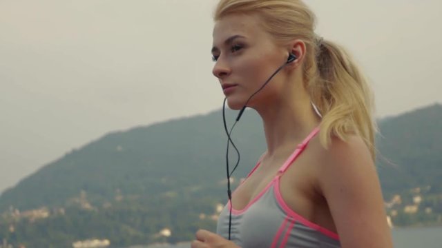 Self-confident blonde is enjoying her morning run and music by the lake, slow motion, picture stabilizer. Natural beauty