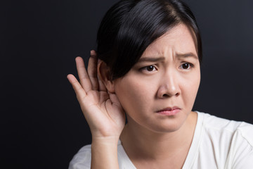 Woman with hand behind her ear and listens carefully