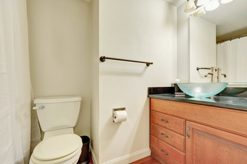 White interior of bathroom with wooden vanity and glass blue washbasin.