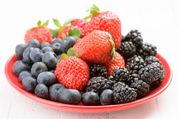 red plate full of ripe berries on white wood