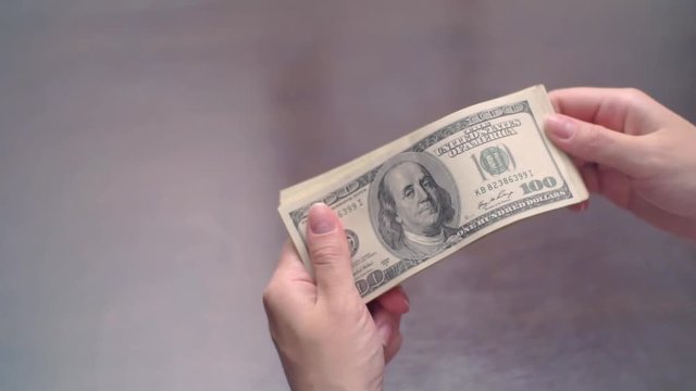 A large stack of hundred dollar bills on a table gradually blows away to nothing.
