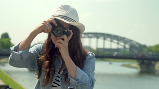 Pretty girl doing photo on vintage camera and smiling next to the river
