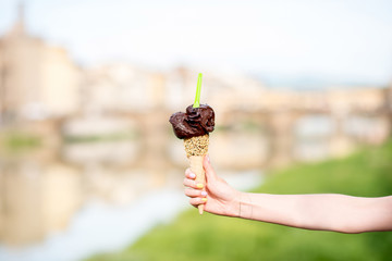 Female hand holding chocolate ice cream in waffle cone on Florence city background. Italian traditional ice cream gelato