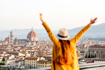 Young female tourist with raised hands looking on the old town of Florence from Michelangelo square in the morning in Italy. Back focus - obrazy, fototapety, plakaty