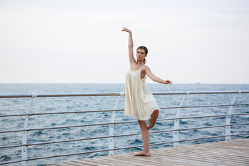 Young beautiful ballerina dancing and posing outside, sea background.