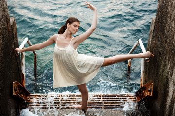 Young beautiful ballerina dancing and posing outside, sea background.