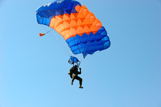 Paraglider flying on colorful parachute in blue clear sky at a bright sunny summer day. Active lifestyle, extreme hobbies