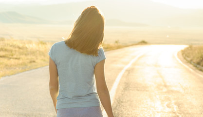 Young woman walking away on an empty road - obrazy, fototapety, plakaty