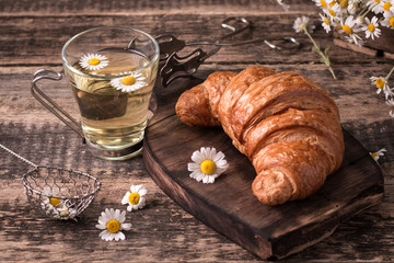 Breakfast with herbal tea and croissant on wooden vintage table