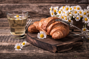 Breakfast with herbal tea and croissant on wooden vintage table