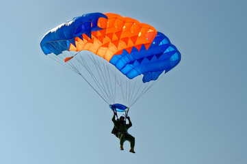 Paraglider flying on colorful parachute in blue clear sky at a bright sunny summer day. Active lifestyle, extreme hobbies