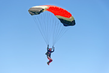 Paraglider flying on colorful parachute in blue clear sky at a bright sunny summer day. Active...