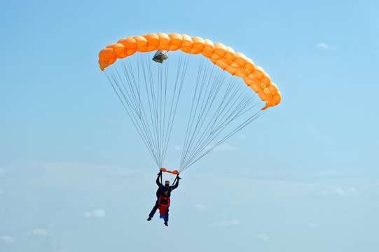 Paraglider flying on orange-colored parachute in blue clear sky at a bright sunny summer day. Active lifestyle, extreme hobbies