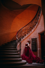 Beauty and shape. Young beautiful woman standing on old round staircase. Blonde girl with tatoo in red cloud dress embracing. Advertising picture
