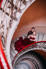 Fototapeta na wymiar Elegant couple at old vintage house and palace with big round stairs. Man in brown shirt. Woman in red cloud dress. 