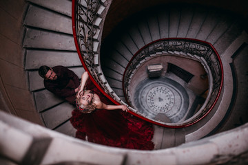 Elegant couple at old vintage house and palace with big round stairs. Man in brown shirt. Woman in red cloud dress. 
