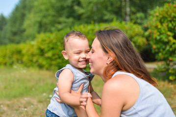 Happy family having fun outdoors. Mother and baby rubbing noses, positive emotions