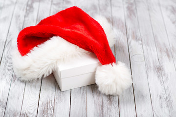Obraz na płótnie Canvas Santa Claus hat over gift box on wooden background. Winter holidays concept.