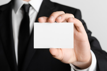 Business Card Mock-Up (85x55mm) - Man in a black suit holding a blank card on a gray background.