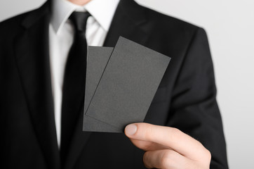 Black Business Card Mock-Up (85x55mm) - Man in a black suit holding a black card on a gray background.