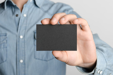Black Business Card Mock-Up (85x55mm) - Man in a denim shirt holding a black card on a gray background.