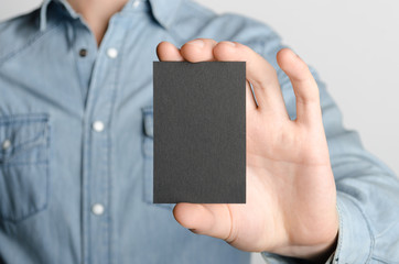 Black Business Card Mock-Up (85x55mm) - Man in a denim shirt holding a black card on a gray background.