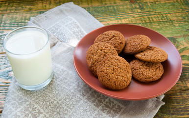 Milk in glass mug with oatmeal cookies on wooden table.