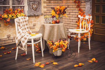 A cozy patio. Autumn leaves lying on the wooden floor, at the center are two white chairs and a...