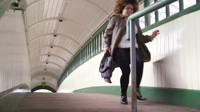 Slow motion video of a woman running over the train station bridge. She has her bag in hand and is eager to catch the train she is late for.