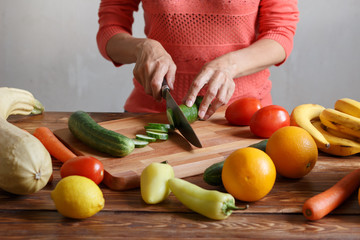 Woman is cutting cucumber for salad on wooden board	