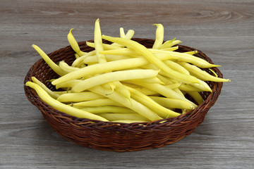Yellow bean pods in wicker bowl, white background