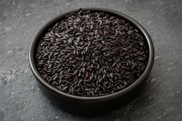 Black rice in a bowl on black background

