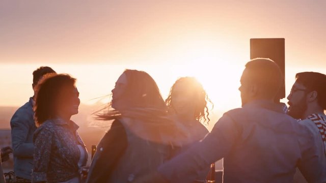 Group of young multi-ethnic people enjoying dancing to the music played by dj at rooftop party at sunset