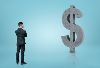 Back view of businessman looking at big concrete dollar sign