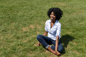 Black woman in a park sitting on lawn happy

