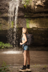 Girl with a backpack against the background of a waterfall. Selective focus.