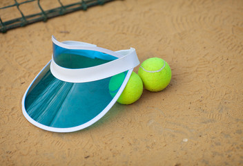Clay tennis court with tennis ball, netting, cap.