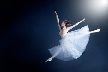 Young ballerina in a beautiful dress is dancing in a dark photostudio