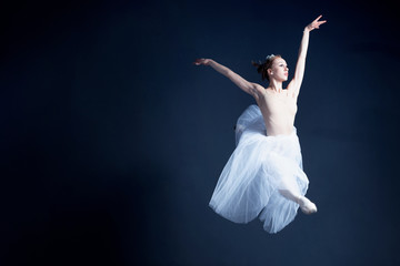 Young ballerina in a beautiful dress is dancing in a dark photostudio