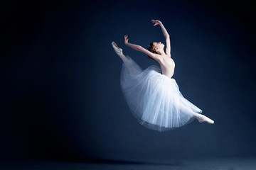 Naklejka premium Young ballerina in a beautiful dress is dancing in a dark photostudio