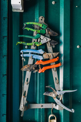 Close-up of colorful rusty pliers hanging on metal rack against of green wall in garage
