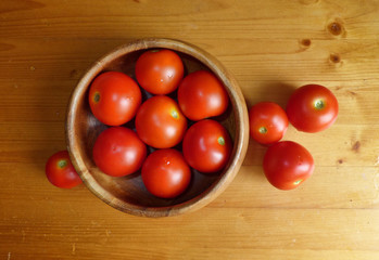 Ripe red tomatoes in the bowl at the wooden table.