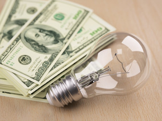 Light bulb in front of dollar bill stack