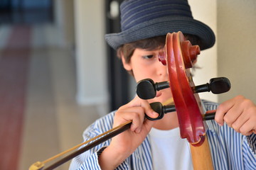 Boy fine tuning large red cello - obrazy, fototapety, plakaty