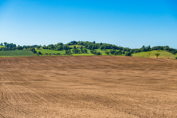 Fototapeta na wymiar Plowed field with green hills, trees and blue sky in the background