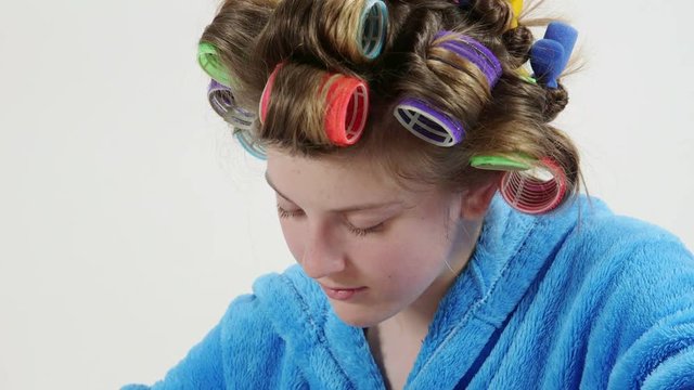 Teenage girl in hair curlers doing manicure at home painting nails with multicolor nail polish