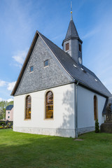 Fototapeta na wymiar Village church in Saxony, Germany, a steeple and slate roof, cloudy sky/Village church
