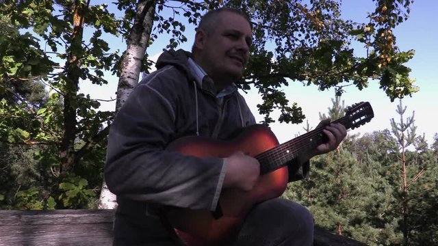 Man playing guitar in wooden tower near trees