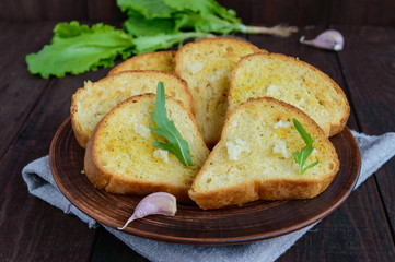 Grilled slices of white bread with garlic and herbs on dark wooden background.